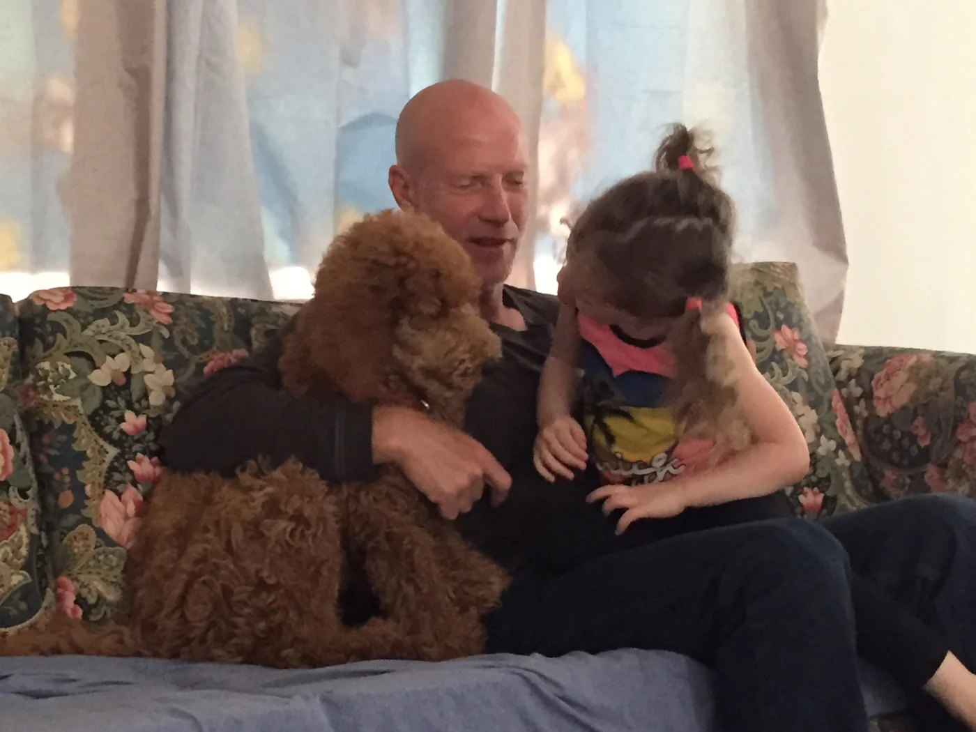 Eran on a sofa with a child and a curly-haired dog